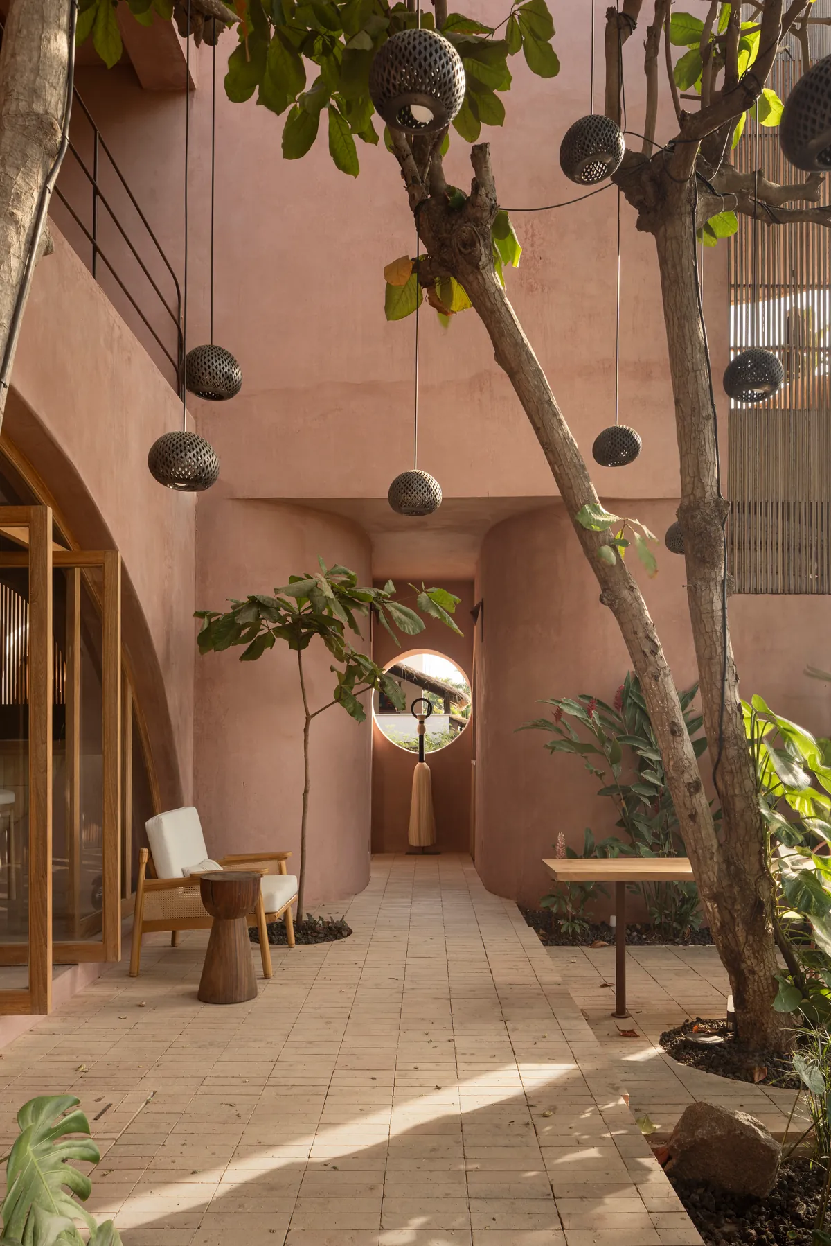 Inner courtyard with curved pink chukum walls, trees growing through the architecture, pierced ceramic lamps and a round window at the end