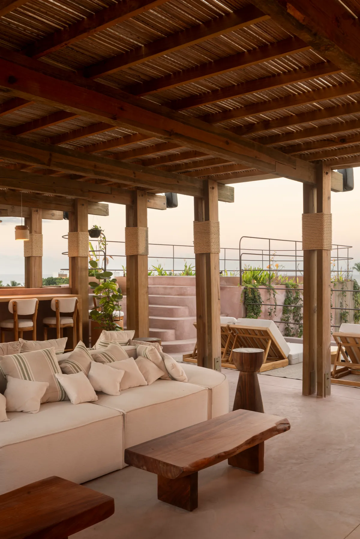 Xiqué’s rooftop under a timber pergola, with rope-wrapped posts, a pale sofa and sun loungers