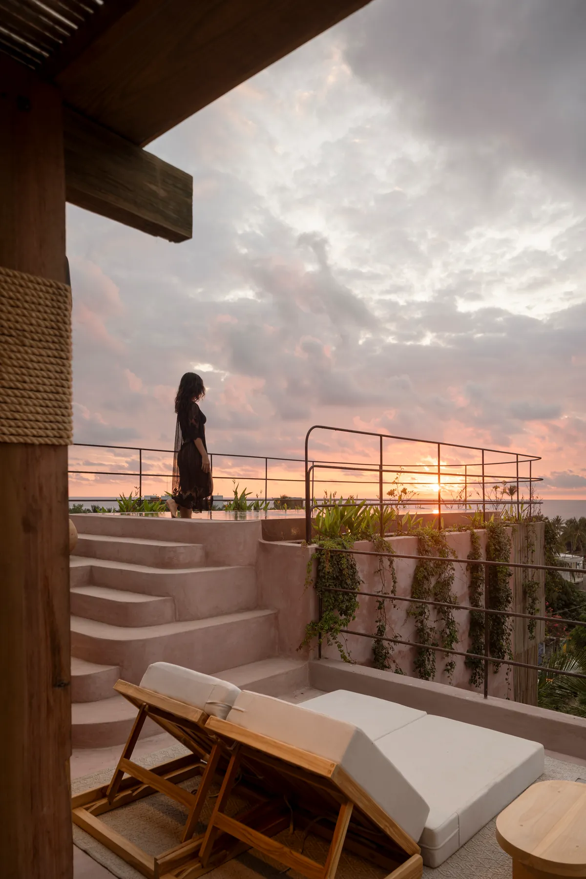 A woman at the top of the rooftop’s chukum steps at sunset, with wooden loungers and the sun setting over the sea