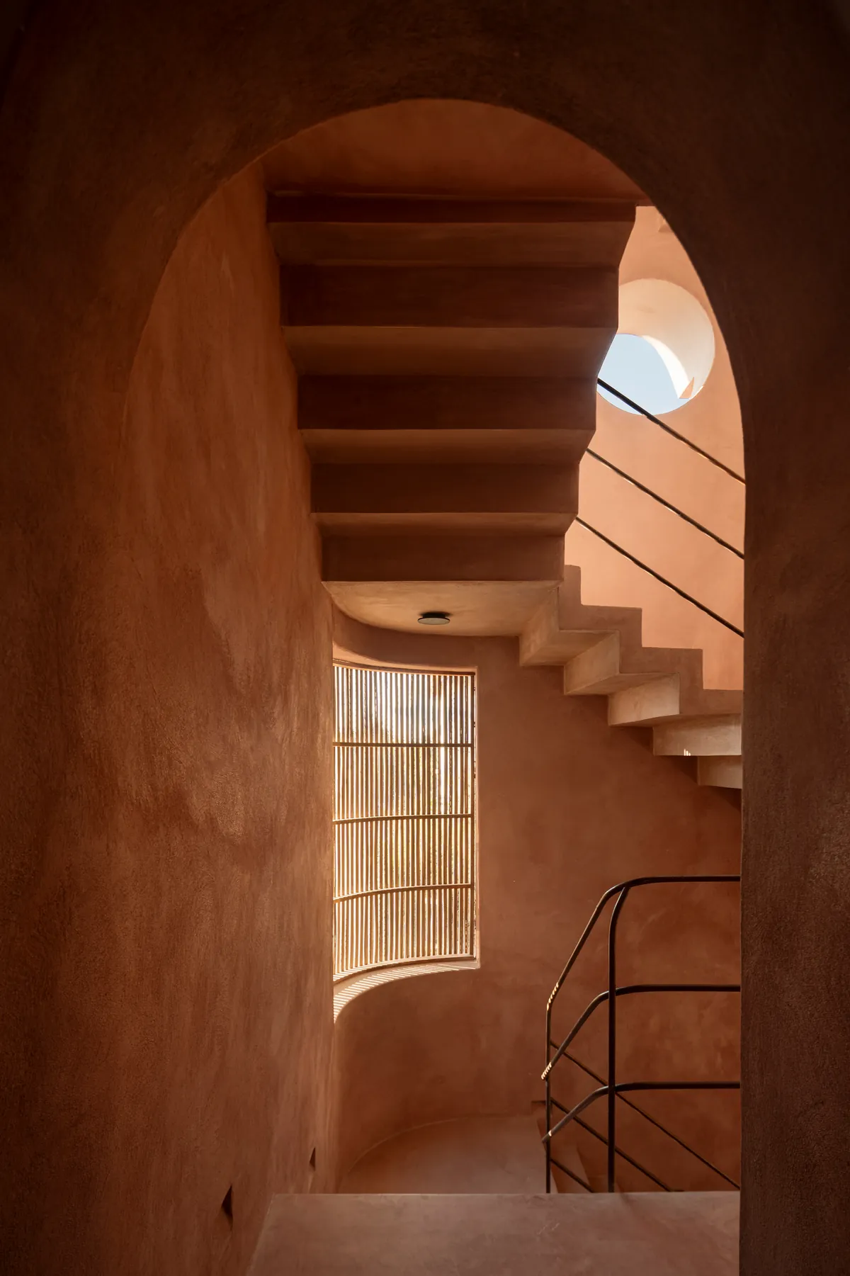 A pink chukum arch framing a concrete staircase, a curved slatted window and a round skylight