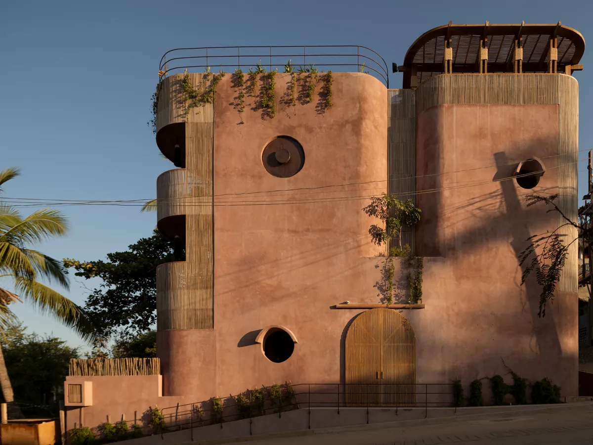 Xiqué on its street in Brisas de Zicatela: curved pink chukum volumes with slatted screens, round windows and an arched wooden door